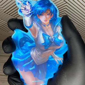 Puede incluir: Una pegatina de personaje de anime azul y blanco con un fondo azul. El personaje es una joven con cabello azul y un uniforme de marinero blanco. Est&aacute; levantando la mano en un gesto de se&ntilde;alamiento. La pegatina est&aacute; rodeada de gotas de agua azules.