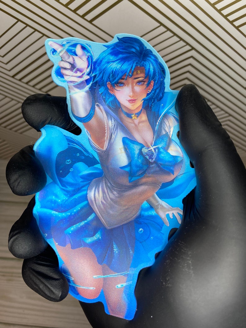 Puede incluir: Una pegatina de personaje de anime azul y blanco con un fondo azul. El personaje es una joven con cabello azul y un uniforme de marinero blanco. Est&aacute; levantando la mano en un gesto de se&ntilde;alamiento. La pegatina est&aacute; rodeada de gotas de agua azules.