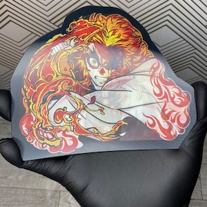 Pu&ograve; includere: Un personaggio anime nero e rosso con capelli arancioni fiammeggianti e una veste bianca. Il personaggio &egrave; raffigurato in una posa dinamica con fiamme che lo circondano.