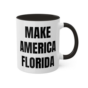 May include: White ceramic coffee mug with a black interior and handle. The mug features the text "MAKE AMERICA FLORIDA" in bold black letters, making it a statement piece for any beverage.