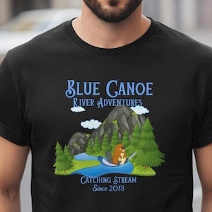 May include: Black t-shirt with a graphic featuring the text "BLUE CANOE RIVER ADVENTURES" above a cartoon scene of a river, mountains, trees, and a beaver. The text "CATCHING STREAM Since 2018" is below the graphic.