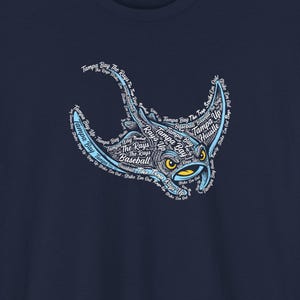以下が含まれることがあります： ネイビーブルーのTシャツ。ライトブルーのオニイトマキエイのデザインで、「Tampa Bay」、「Rays」、「Baseball」などの文字で構成されています。オニイトマキエイは黄色い目をしています。背景には野球場が描かれています。
