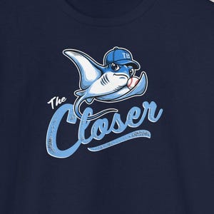 Può includere: T-shirt blu navy con un cartone animato di una manta che indossa un berretto da baseball. Il testo "The Closer" è scritto in blu chiaro. Il design della maglietta è probabilmente legato a una squadra di baseball.