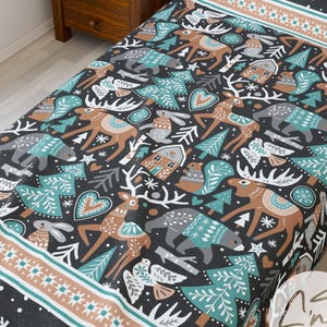 Könnte beinhalten: Eine schwarz-weiß gemusterte Bettdecke mit Winterwald-Motiv. Das Design umfasst Hirsche, Bären, Bäume und Häuser in Braun-, Türkis- und Grautönen. Der Rand weist ein geometrisches Muster und Schneeflocken auf.