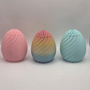 Pu&ograve; includere: Tre oggetti decorativi a forma di uovo dai colori pastello. Le uova hanno un design a spirale e sono colorate di rosa, arcobaleno e blu. Le uova sono probabilmente per le decorazioni pasquali o primaverili.