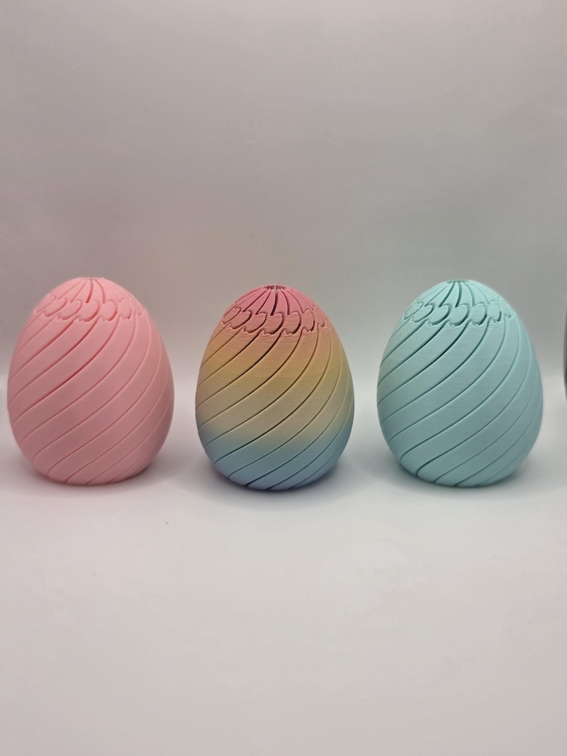 Pu&ograve; includere: Tre oggetti decorativi a forma di uovo dai colori pastello. Le uova hanno un design a spirale e sono colorate di rosa, arcobaleno e blu. Le uova sono probabilmente per le decorazioni pasquali o primaverili.