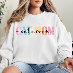 a woman wearing a white sweatshirt that says cat mom