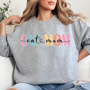a woman sitting on a couch wearing a grey sweatshirt with the word catatonn