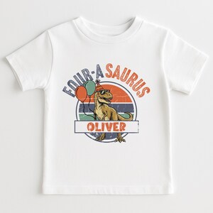 Front view of a "Four-a-Saurus" birthday sweatshirt for a four-year-old boy. The design uses earthy tones like mustard yellow, olive green, and rust orange against a neutral beige fabric. This preppy and modern garment is perfect for a rustic or boho-themed dinosaur birthday party and provides a trendy look for toddlers in 2026.