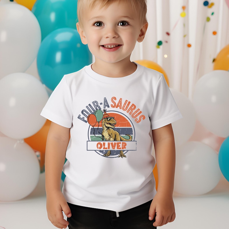 A lifestyle mockup of a toddler hoodie featuring the custom "Oliver" dinosaur design. The T-Rex is shown holding orange and green balloons, adding to the festive atmosphere of a fourth birthday. The retro sunset background adds a vintage feel to the high-quality print, appealing to parents looking for aesthetic and personalized kids' apparel on Etsy.