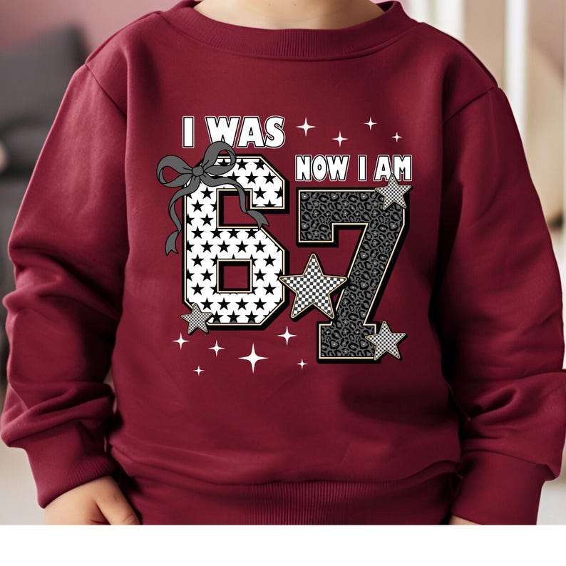 Front view of a pink youth t-shirt displayed on a model. The central graphic celebrates a 7th birthday with the phrase "I Was 6 Now I Am 7". The font is bold and playful. The design incorporates trendy elements like checkered patterns and sparkles, appealing to modern trends in children's clothing. It serves as a great keepsake for marking the age of seven.