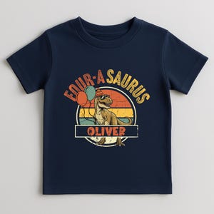 A mockup of the "Fourasaurus" design on a light beige toddler t-shirt. The personalization section at the bottom is highlighted with the name "OLIVER." The illustration includes green and orange balloons and a detailed T-Rex, signifying the big transition to being four years old. The fabric looks soft and comfortable for all-day birthday play.