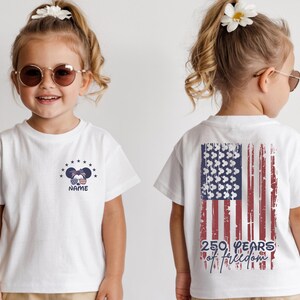 A young girl wearing a white t-shirt with an American flag design and the text "250 years of freedom" printed on the back.