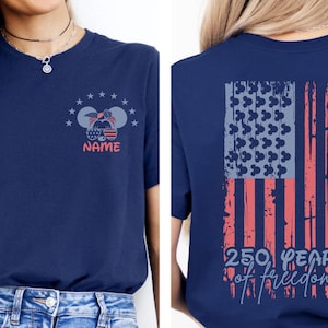 A woman wearing a navy blue t-shirt with a graphic design on the back featuring an American flag and the text "250 years of freedom".