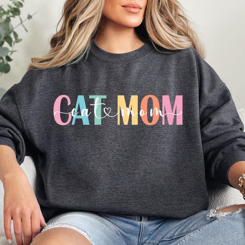 a woman sitting on a couch wearing a sweatshirt that says cat mom