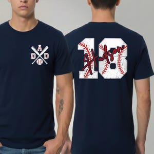 May include: Navy blue baseball t-shirt with white and red graphics. The front features crossed baseball bats, a baseball, and the word "DAD". The back displays the name "Hudson" and the number "18" in a baseball-themed design.