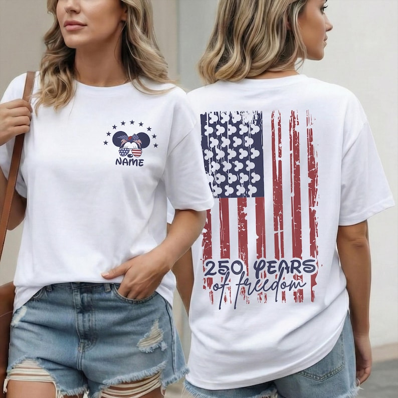 A white t-shirt featuring a double-sided Disney patriotic design. The front left chest shows a small Mickey Mouse head wearing USA flag sunglasses and a bandana with the custom name "NAME". The back features a large, distressed American flag graphic.