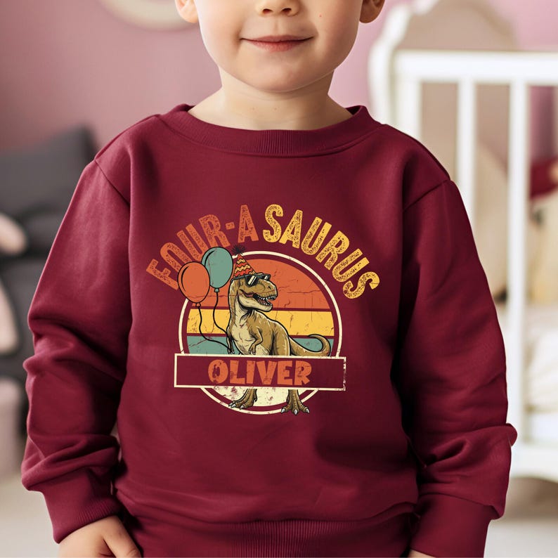 Close-up on the typography and graphics of a personalized dinosaur hoodie for boys. The phrase "FOUR-A-SAURUS" is a fun play on words for a 4th birthday. The print is sharp and professional, showing the fine details of the T-Rex's scales and the reflections on its cool black sunglasses. Perfect for a dinosaur-loving four-year-old.