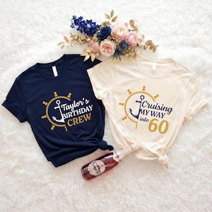 May include: Two t-shirts with nautical-themed designs. One navy blue shirt says "Taylor's BIRTHDAY CREW" and the other is cream-colored and says "Cruising MY WAY into 60". A bottle of wine and flowers are also in the image.