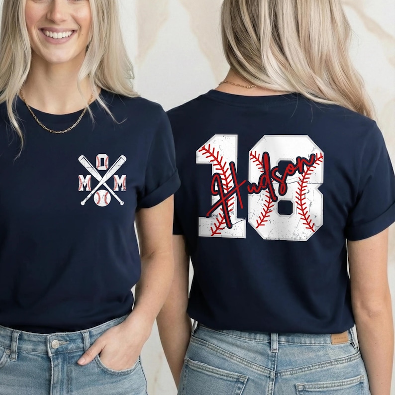A woman wearing a navy blue t-shirt with a baseball design and the number 18 on the back, standing in front of a beige wall.