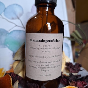 Op de afbeelding: Een bruine glazen fles VIT C SERUM met een zwarte druppelaar. Het etiket luidt "Myamazingcraftideas" en bevat ingrediënten en instructies. De fles bevat 120 ml serum. De fles is omgeven door gedroogde sinaasappelschillen en andere botanische producten.