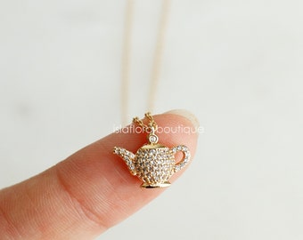 May include: A gold necklace with a small, sparkling teapot pendant. The teapot is covered in clear crystals.