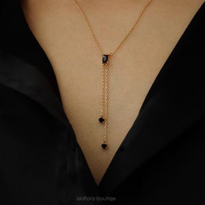 May include: A gold chain necklace with a black rectangular pendant and two smaller black round stones hanging from the bottom.