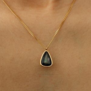 May include: A gold chain necklace with a teardrop-shaped pendant. The pendant is black with a pearlescent sheen.