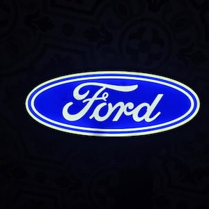 May include: A blue oval with a white border and the word "Ford" in white script. The logo is set against a dark background with a subtle pattern.
