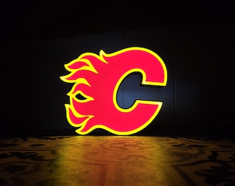 May include: A neon sign in the shape of the letter "C" with a flame design, in red and yellow. The sign is illuminated against a dark background, with a patterned surface below.