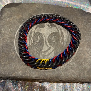 May include: A black, red, and blue chainmail bracelet with a yellow accent.