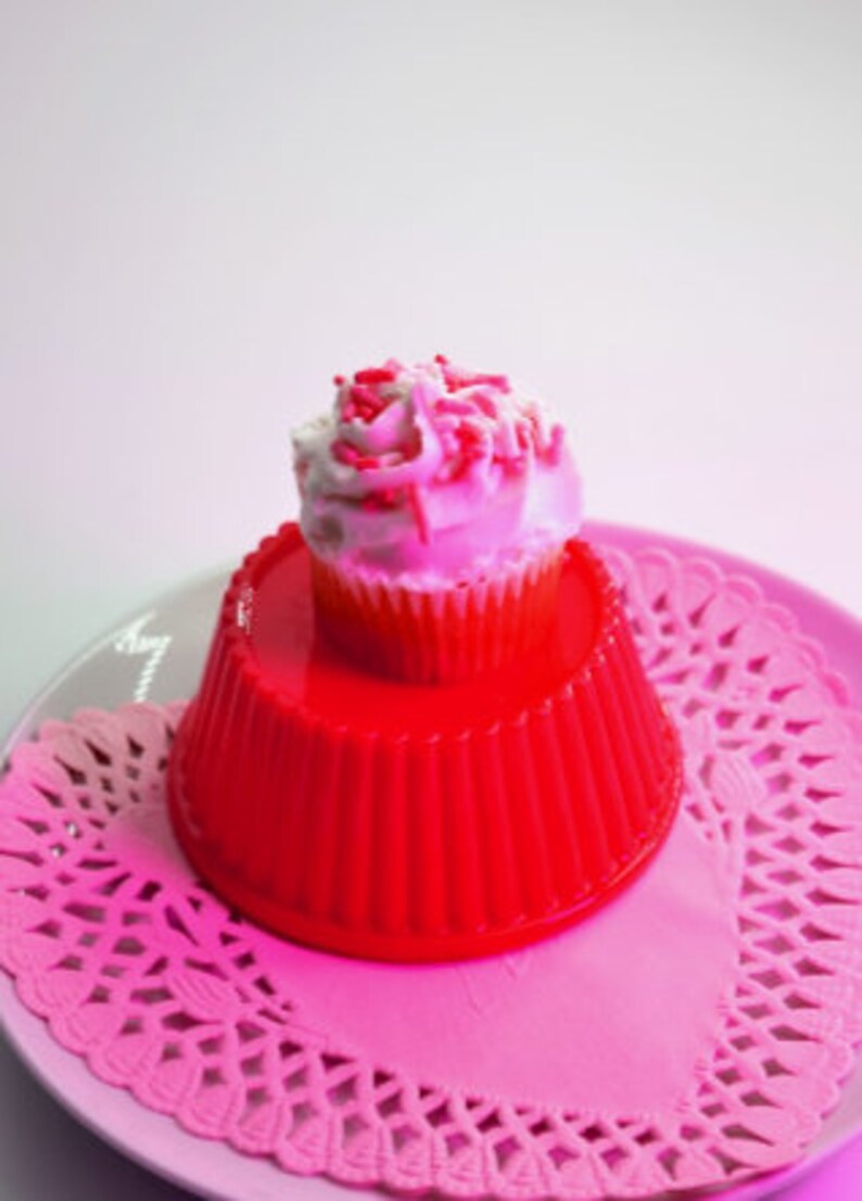 May include: A red gelatin dessert mold with a white cupcake topped with pink and white frosting and pink sprinkles.