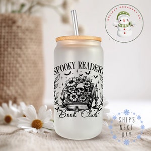 Puede incluir: Un vaso de vidrio esmerilado con un dise&ntilde;o en blanco y negro de una calavera, flores y un libro con el texto "Spooky Reader Book Club". El vaso tiene una tapa de bamb&uacute; y una pajita transparente.