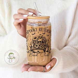 Puede incluir: Un vaso de vidrio transparente con tapa de bamb&uacute; y una pajita. El vaso tiene un dise&ntilde;o en blanco y negro de una calavera, flores, velas y un libro con el texto "Spooky Reader Book Club".