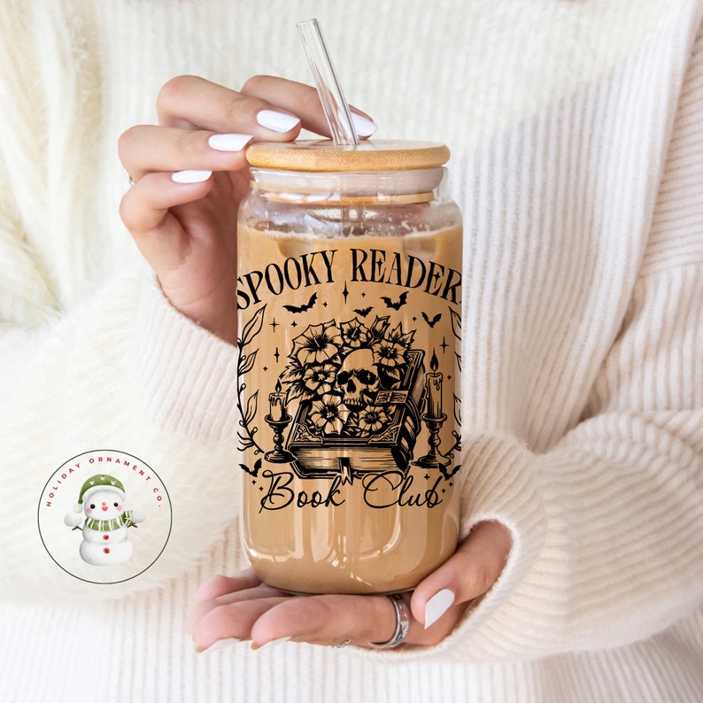 Puede incluir: Un vaso de vidrio transparente con tapa de bamb&uacute; y una pajita. El vaso tiene un dise&ntilde;o en blanco y negro de una calavera, flores, velas y un libro con el texto "Spooky Reader Book Club".