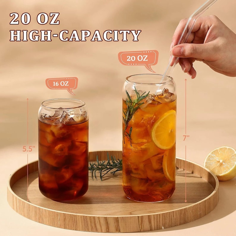 May include: Two clear glass tumblers filled with iced tea and garnishes, one 16 oz and the other 20 oz. The taller glass is 7 inches high. A clear glass straw is being inserted into the larger glass. The text reads "20 OZ HIGH-CAPACITY".