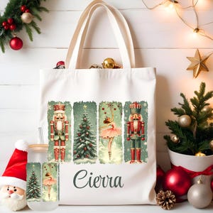 Könnte beinhalten: Weiße Canvas-Tragetasche mit einem Weihnachtsmotiv mit einer Ballerina, einem Nussknacker und einem Weihnachtsbaum. Die Tasche hat einen personalisierten Namen "Cierra", der auf der Vorderseite aufgedruckt ist.