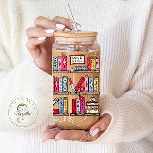 May include: A clear glass tumbler with a bamboo lid and a straw. The tumbler has a graphic of a bookshelf with colorful books and the text "GOOD GIRL" on one of the books.