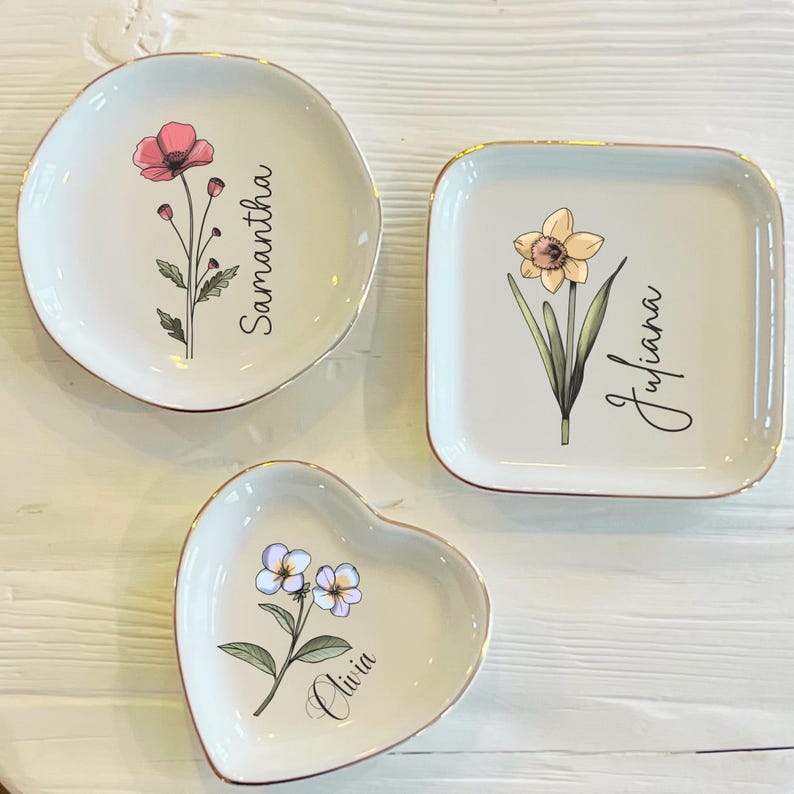 May include: Three ceramic trinket dishes with gold trim. The dishes are shaped like a heart, a square, and a circle. Each dish features a different floral design and a name: Olivia, Juliana, and Samantha.