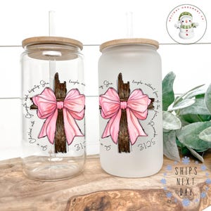 May include: Two glass tumblers with bamboo lids and straws. Each tumbler features a cross design with a pink bow and script. One is clear, the other frosted. Text includes "She laughs without fear of the future" and "31:25".