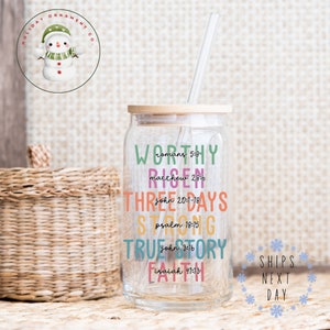 May include: A clear glass tumbler with a wooden lid and a straw. The tumbler has colorful text that reads "WORTHY romans 5:8 RISEN matthew 28:6 THREE DAYS john 20:1-18 STRONG psalm 18:15 TRUE STORY john 3:16 FAITH isaiah 41:13".
