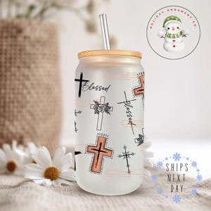 May include: A frosted glass tumbler with a wooden lid and a straw. The tumbler has a pattern of crosses and the word "blessed" repeated on it. The crosses are in black and the word "blessed" is in a pink color.
