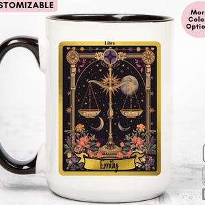May include: White ceramic mug with a black handle and rim. The mug features a Libra zodiac design with a gold scale, flowers, and a moon on a black background. The name "Emily" is printed on a gold banner.