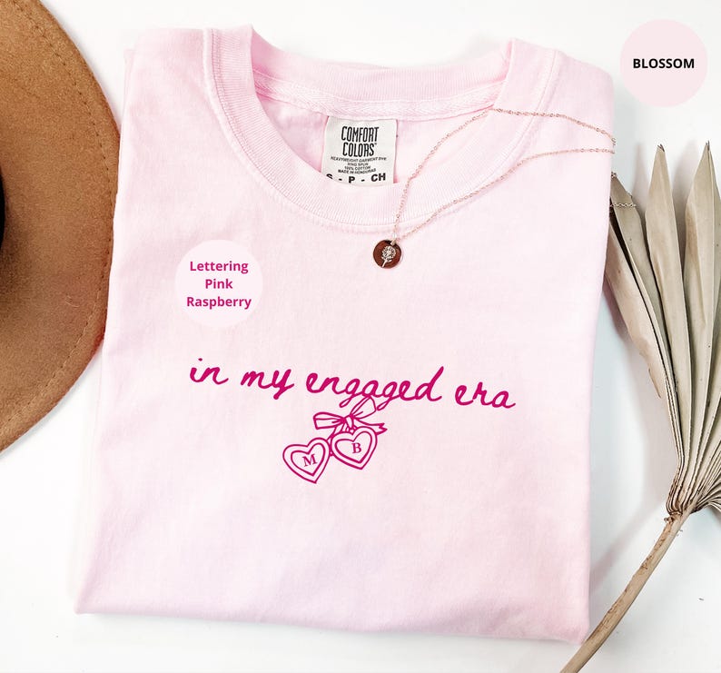 Blossom Comfort Colors® t-shirt with custom raspberry text "in my engaged era" and heart lock graphic, perfect for brides-to-be and engagement gifts.