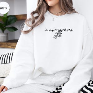 White Sweater with custom black text "in my engaged era" and heart lock graphic, perfect for brides-to-be and engagement gifts.