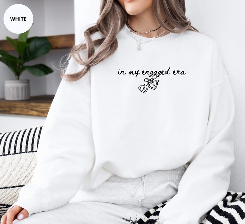 White Sweater with custom black text "in my engaged era" and heart lock graphic, perfect for brides-to-be and engagement gifts.