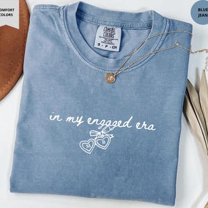 Blue Jean Comfort Colors® t-shirt with custom white text "in my engaged era" and heart lock graphic, perfect for brides-to-be and engagement gifts.