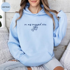 Light Blue Comfy Hoodie with custom navy text "in my engaged era" and heart lock graphic, perfect for brides-to-be and engagement gifts.