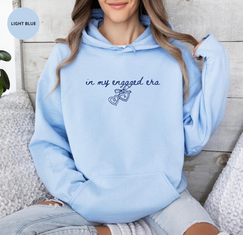 Light Blue Comfy Hoodie with custom navy text "in my engaged era" and heart lock graphic, perfect for brides-to-be and engagement gifts.