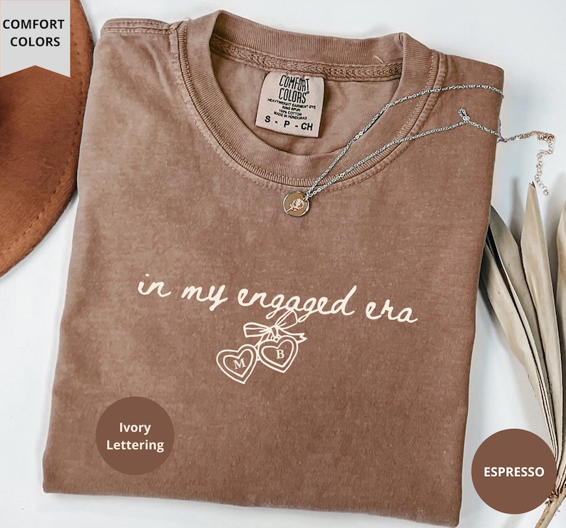 Espresso Comfort Colors® t-shirt with custom ivory text "in my engaged era" and heart lock graphic, perfect for brides-to-be and engagement gifts.